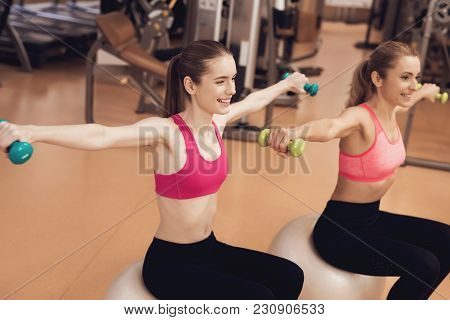 Mother And Daughter In Sportswear Sitting Doing Exercises With Dumbbells At The Gym. They Look Happy