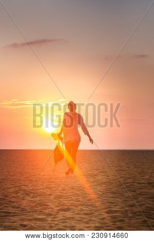 A Girl Is Walking Along The Beach Towards The Sun