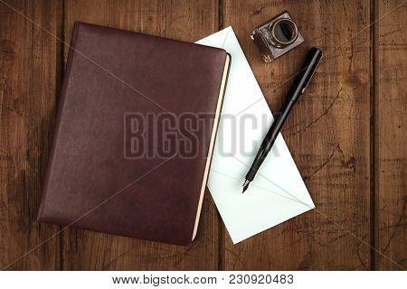 An Overhead Photo Of A Leather Bound Journal, A Blue Envelope, An Ink Well And Pen, Shot From Above 