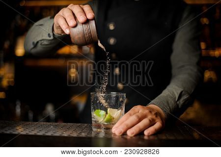 Bartender Pouring Cane Sugar Into The Cocktail Glass With Slices Of Lime On The Bar Counter