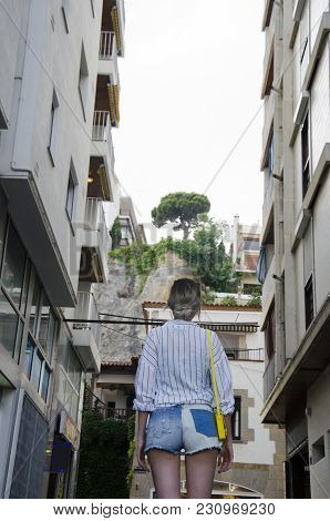Young Woman In A White Shirt And With A Yellow Little Bag Tourist Walking On The Streent Of Lloret D