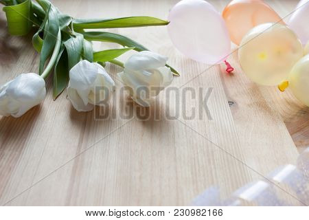 Three White Tulips And Small Air Balloons On A Light Wooden Background