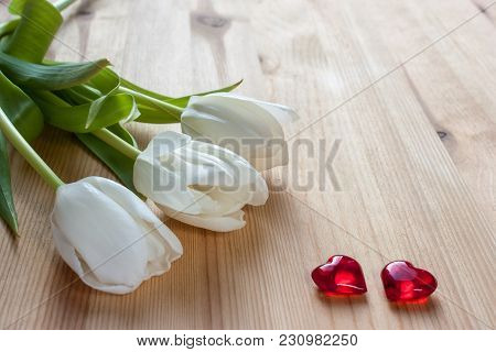 Three White Tulips And Two Red Hearts On A Wooden Background