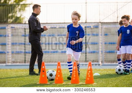 Young Happy Blonde Soccer Player Running With Ball On Training. Coach Of Youth Football Team Explain