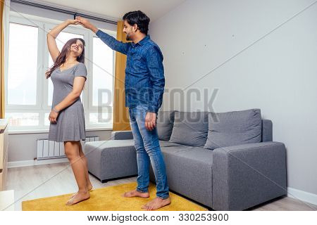 Happy Indian Couple Dancing Together In New Light Apartment With Design Repair:gray Sofa, Yellow Cur
