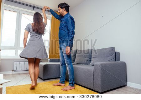 Happy Indian Couple Dancing Together In New Light Apartment With Design Repair:gray Sofa, Yellow Cur