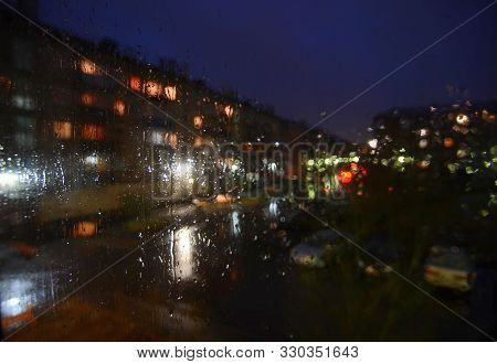 Night Rainy Sityscape Outside The Window Pane - Defocused Blurred Background With Water Drops On Gla