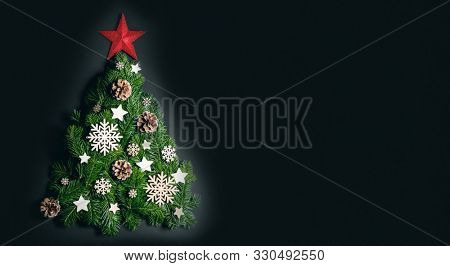 Christmas tree made of natural spruce branches deecor with red star on black background, flat lay card with copy space