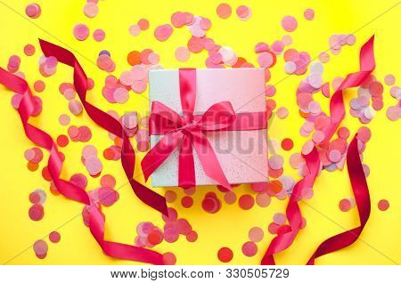 Giftbox Tied With Pink Color Ribbon On Bright Yellow Background With Sparklets And Confetti. Flat La