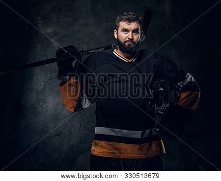 Portrait Of Brutal Bearded Man In Hockey Player Uniform At Dark Photo Studio.