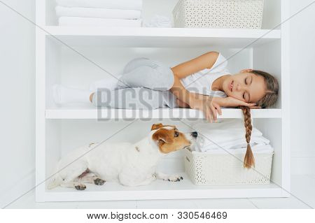 Sleepy Little Girl Feels Comfortable As Lies On White Shelf Dressed In Casual Clothing Tired After W