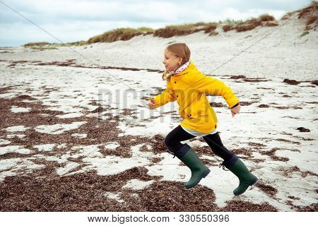 Cheerful Little Girl Running On Water Of Baltic Sea In Rubber Boots At Windy Weather