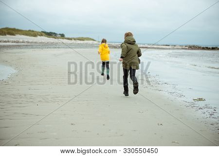 Two Happy Children Running And Jumping On Water Of Baltic Sea In Rubber Boots At Windy Weather