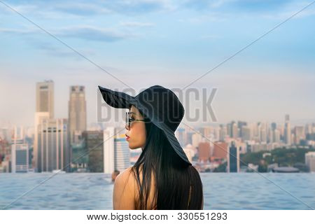 Young woman in a roof top swimming pool, infinity pool with beautiful city view. Vacation in Singapore.