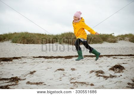 Cheerful Little Girl Running On Water Of Baltic Sea In Rubber Boots At Cold Weather