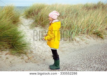 Cheerful Little Girl Staying On Beach Of Baltic Sea At Windy Weather