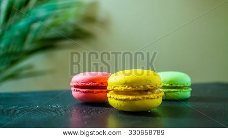 Three Macaroons Cookies On A Dark Background With A Palm Tree At The Back. Copy Space.