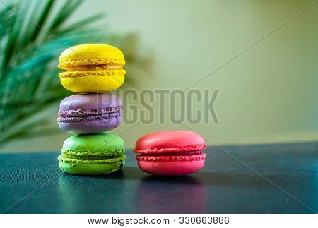 Four Macaroons Cookies On A Dark Background With A Palm Tree At The Back. Copy Space.