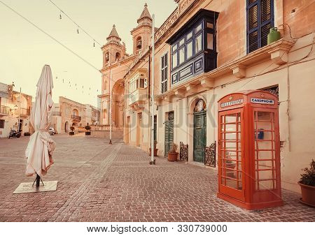 Marsaxlokk, Malta: Traditional Red Color Phone Booth On Historical Square With Church And Beautiful 
