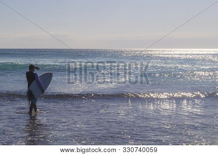 Male Surfer Entering The Sea With His Board.ready For A Great Surfing Day.