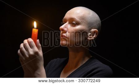 Portrait Of A Bald Woman With A Candle On A Black Background. Copy Space