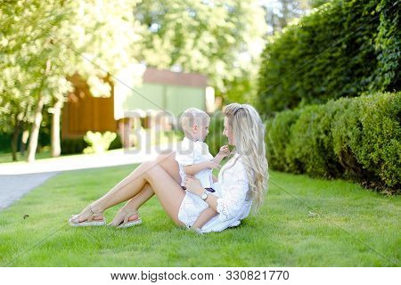 Young Euopean Mother Sitting With Little Baby On Grass In Yard.