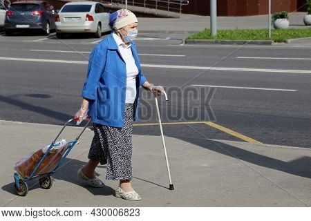 Moscow, Russia - August 2021: Elderly Woman In Mask And Protective Gloves Walking With A Cane And Ro