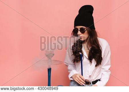 A Young Woman In A Hipster Image Smokes A Hookah, Sheesha And Enjoys Smoking.
