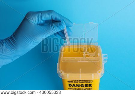 Doctor Throwing Used Syringe Needle Into Sharps Container On Light Blue Background, Closeup