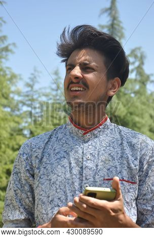 Closeup Portrait Of A Indian Good Looking Young Guy Standing Outdoor In Nature And Holding Mobile Ph