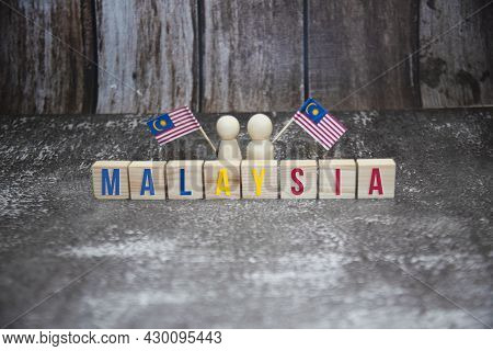 Malaysia Word On Wooden Block With Two Wooden Doll Holding Malaysia Mini Flag.