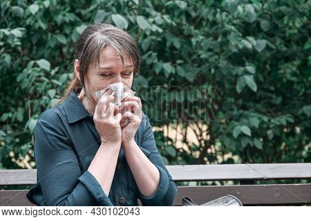 Health Care Concept, Sick Woman Blew Her Nose Into A Paper Napkin While Sitting On A Park Bench.