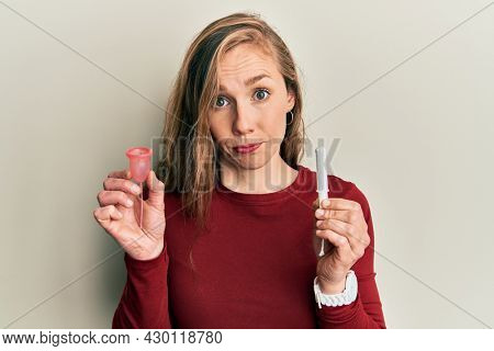 Young blonde woman holding menstrual cup and tampon skeptic and nervous, frowning upset because of problem. negative person. 