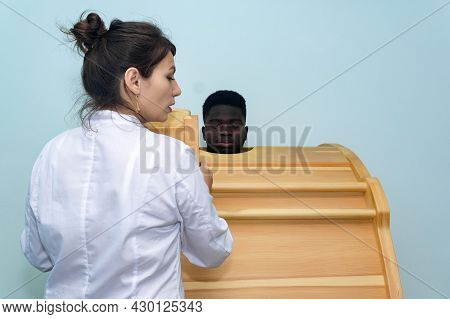 Young Black Man Takes A Therapy Session In A Phyto Barrel Under The Supervision Of Female Doctor