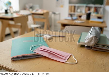 Protective mask on copybook and textile pencilbox on wooden desk in classroom