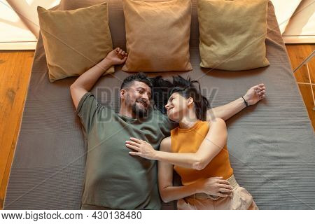 Young restful couple lying on bed with three cushions during summer vacation