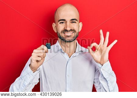 Young bald man holding sdxc card doing ok sign with fingers, smiling friendly gesturing excellent symbol 