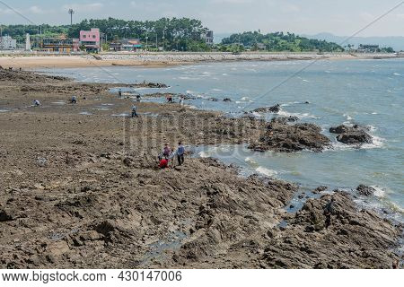 Seosan, South Korea; August 4, 2021: Unidentified People Enjoying Day Out On Stony Ocean Beach.