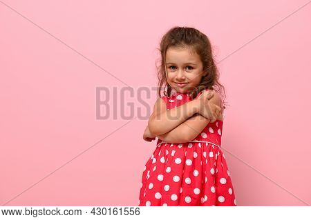Beautiful Preschool 4 Years Kid Girl Shyly Hugging Herself, Cute Smiling Posing On Camera Against Pi