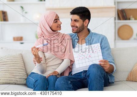 Happy Arab Couple Planning Pregnancy, Holding Positive Pregnancy Test And Ovulation Calendar, Sittin