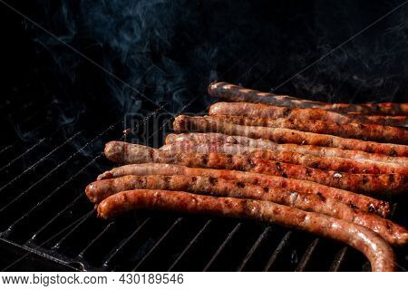 Roasted Bbq Sausages With Grillmarks Cooking On Grill Barbecue With Smoke. Outdoor Summertime Meal P