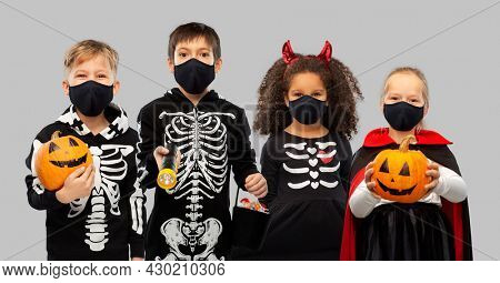holiday, health and pandemic concept - children in halloween costumes and black reusable masks trick-or-treating over grey background