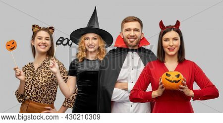 holiday, theme party and people concept - happy smiling friends in halloween costumes over grey background