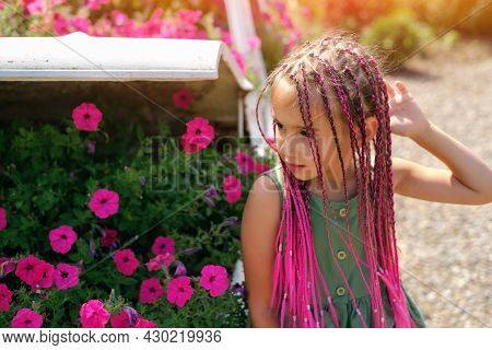 A Beautiful Cute Girl With Pink Afro-pigtails From Kanekalon Stands In Front Of A Flower Bed With Fl