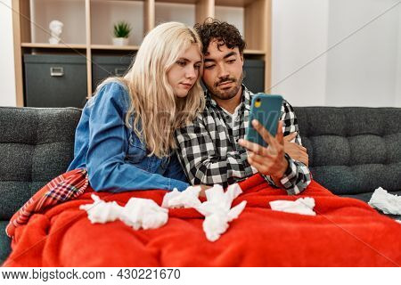 Young ill couple having medical teleconsultation using smartphone at home.