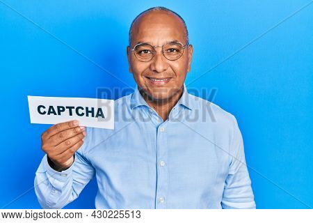 Middle age latin man holding captcha message paper looking positive and happy standing and smiling with a confident smile showing teeth 
