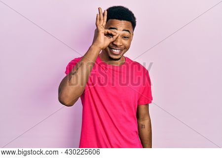 Young african american man wearing casua t shirt doing ok gesture with hand smiling, eye looking through fingers with happy face. 