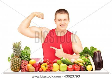 Passen Sie jungen Mann zeigt seine Muskeln hinter einem Haufen von Obst und Gemüse, isolated on white backgroun