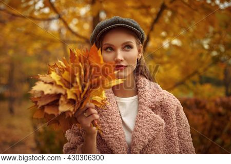 Dreammy beautiful young woman walks in the autumn park with a bouquet of yellow maple leaves. 