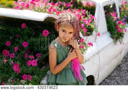 A Girl In A Dress With Pink Zizi Pigtails From Kanekalon Stands At A Decorative Car With Flowers Gro